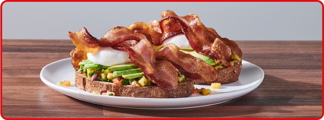 An open-faced breakfast sandwich featuring eggs and piled high with crispy bacon. 