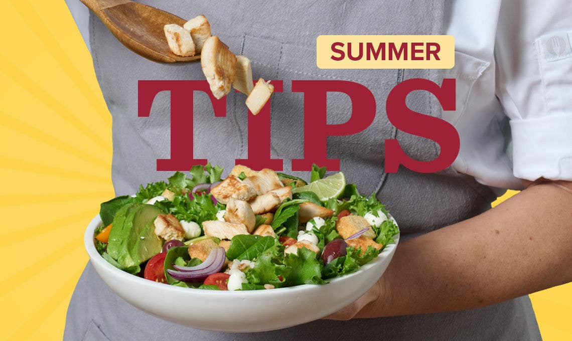 chef’s hands holding a white bowl with salad and adding roasted chicken from wooden spoon