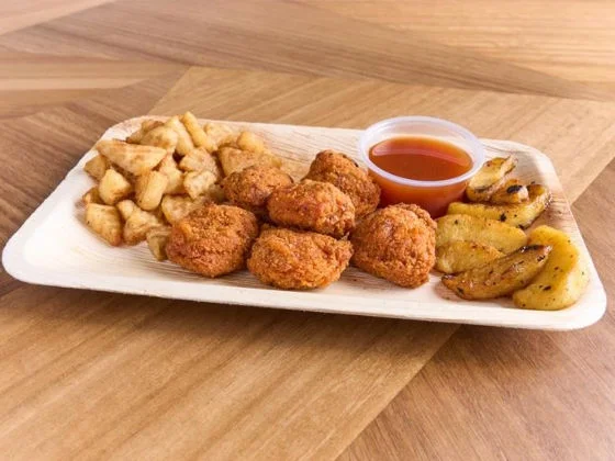 Fried steak bites with waffles, dipping sauce, roasted potatoes on a wooden plate