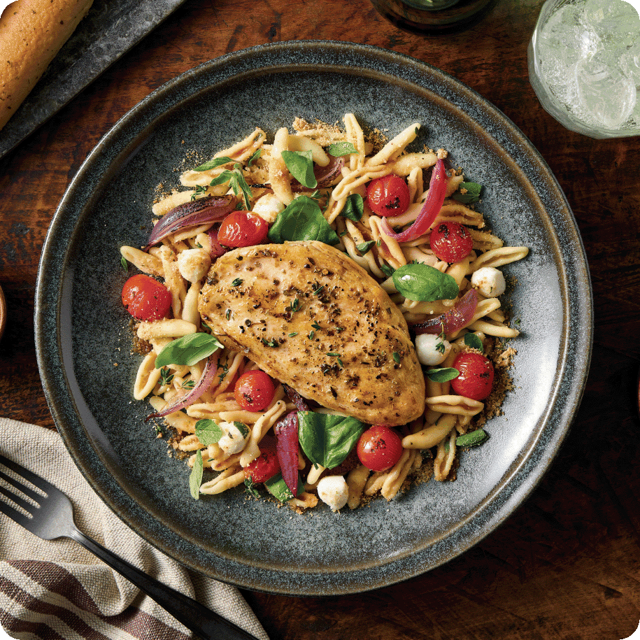 hicken breast resting on top of pasta and fresh cherry tomatoes and garnished with basil   