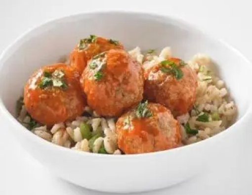 Bowls of chicken meatballs covered in buffalo sauce and served over seasoned brown rice 
