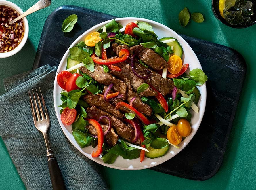 sliced beef on a bed of watercress, cherry tomatoes, papaya, red bell pepper slices and red onions 
