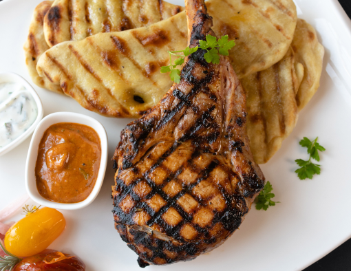 Grilled pork tomahawk on plate with sauces, tomatoes and onions