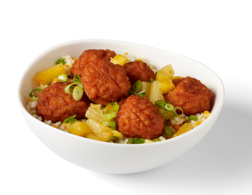A bowl of breaded boneless wings over brown rice, pineapples and scallions 