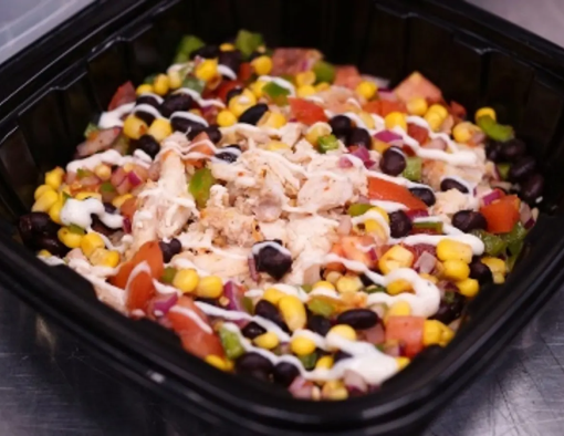 To-go container with pulled chicken mixed with black bean and corn salsa over a bed of rice with cheese sauce drizzle 