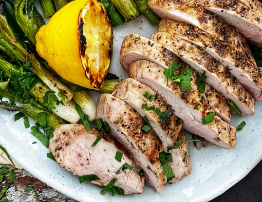 Grilled pork tenderloin cut up, next to a grilled lemon and asparagus