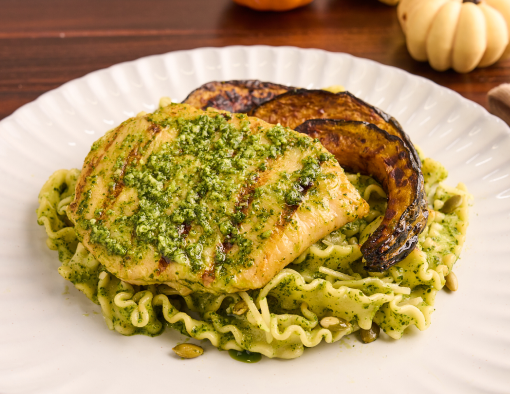 Grilled chicken on mafaldine pasta with pepita pesto, roasted squash, and arugula on a white plate