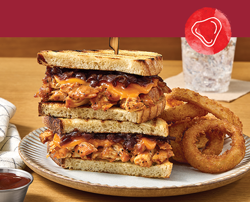 Stacked smoked chicken melt sandwich with barbecue sauce and melted cheese on toasted bread, served with crispy onion rings on a plate
