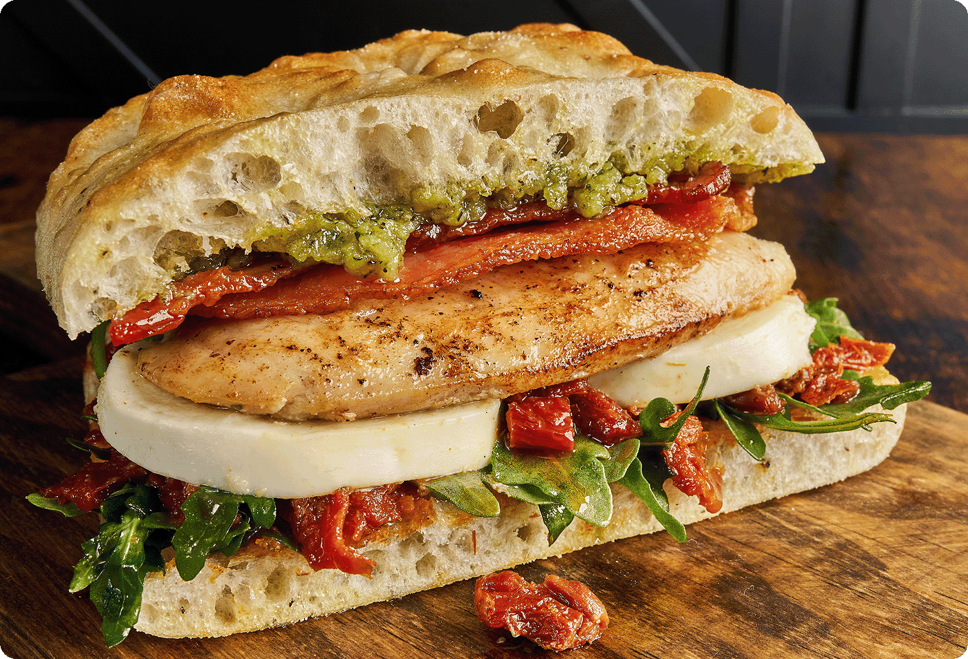 A hearty grilled chicken sandwich with tomatoes, pesto, bacon and fresh mozzarella on focaccia bread    