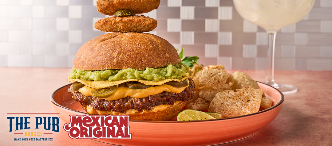 A plate with a burger featuring a ground beef patty topped with melted cheese, guacamole and a tostada on a bun topped with skewered jalapeño poppers    
