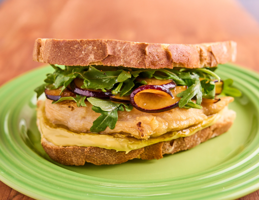 Grilled chicken on sourdough with pistachio butter, marinated plums, and arugula on a green plate, on a wooden surface