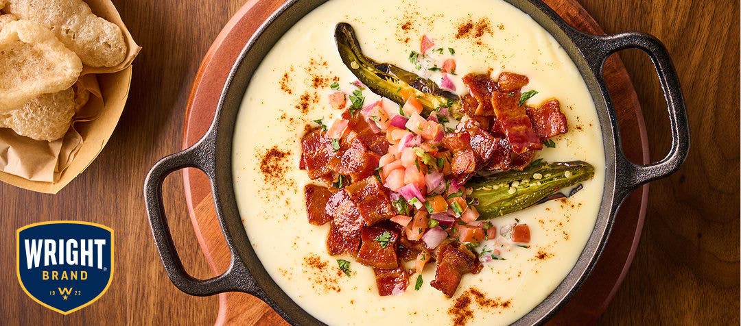 skillet filled with queso dip, chopped bacon, halved jalapeños and pico de gallo 