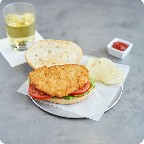 Crispy chicken breast sandwich with lettuce and tomato, served with potato chips.