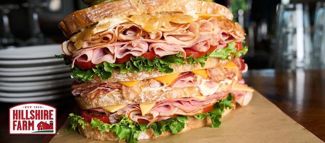 An enormous sandwich stacked with several layers of meat, cheese, bread, tomatoes and lettuce 