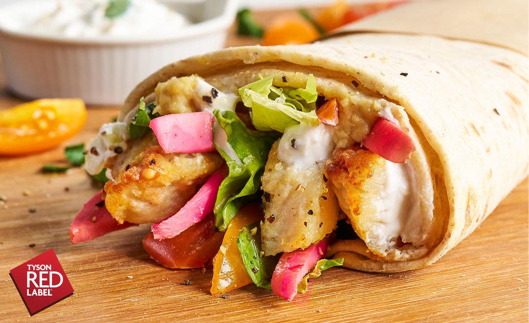 Close up of the open-end of a wrap with grilled chicken, tomatoes, lettuce and pickled turnips spilling out of the tortilla   