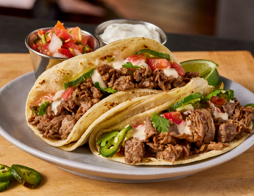 Two plated carne asada soft tacos with pico and sour cream