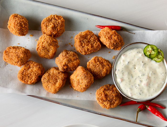Crispy fried beef bites on a parchment-lined tray with creamy dipping sauce, sliced jalapeños, and red chili peppers
