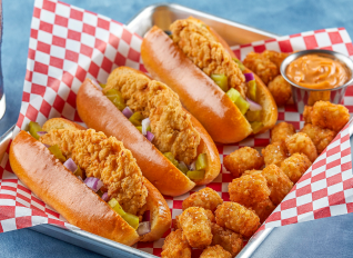 Fried chicken sandwiches and tater tots with sauce on a tray with red checkered paper