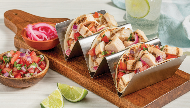 Grilled chicken tacos with fresh salsa and pickled onions, served with lime wedges on a wooden board