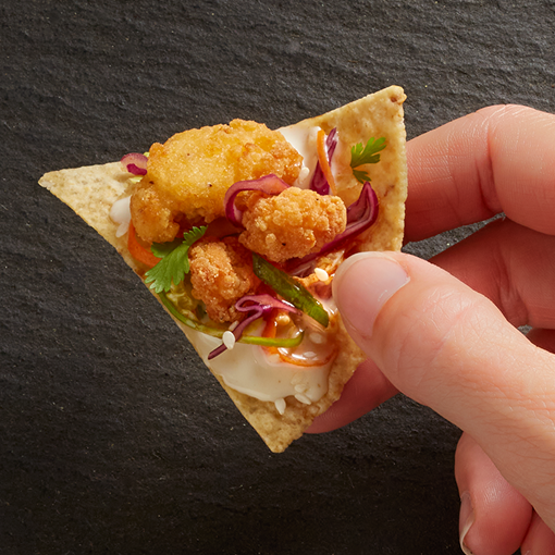 nacho topped with Tyson Mini Whole Muscle Chicken Bites, slaw, and sauce