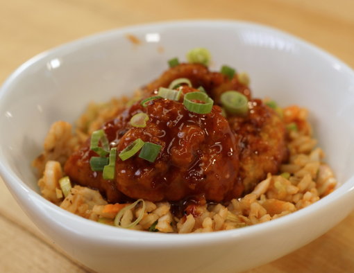 A bowl of breaded boneless chicken wings in barbecue sauce over a bed of rice and slaw 