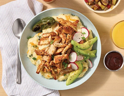 Tyson® Pitmaster Naturally Smoked Sweet Heat Dry Rub Chicken Thigh Pieces over roasted jalapeño cheese grits with avocado slices and radish coins