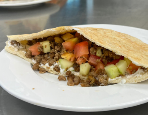 Pita pocket stuffed with beef crumbles, creamy yogurt, diced tomatoes and cucumbers on a plate 