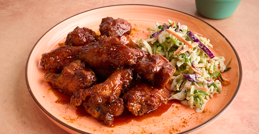 Saucy chicken wings and coleslaw on a peach plate with a small bowl of creamy dipping sauce