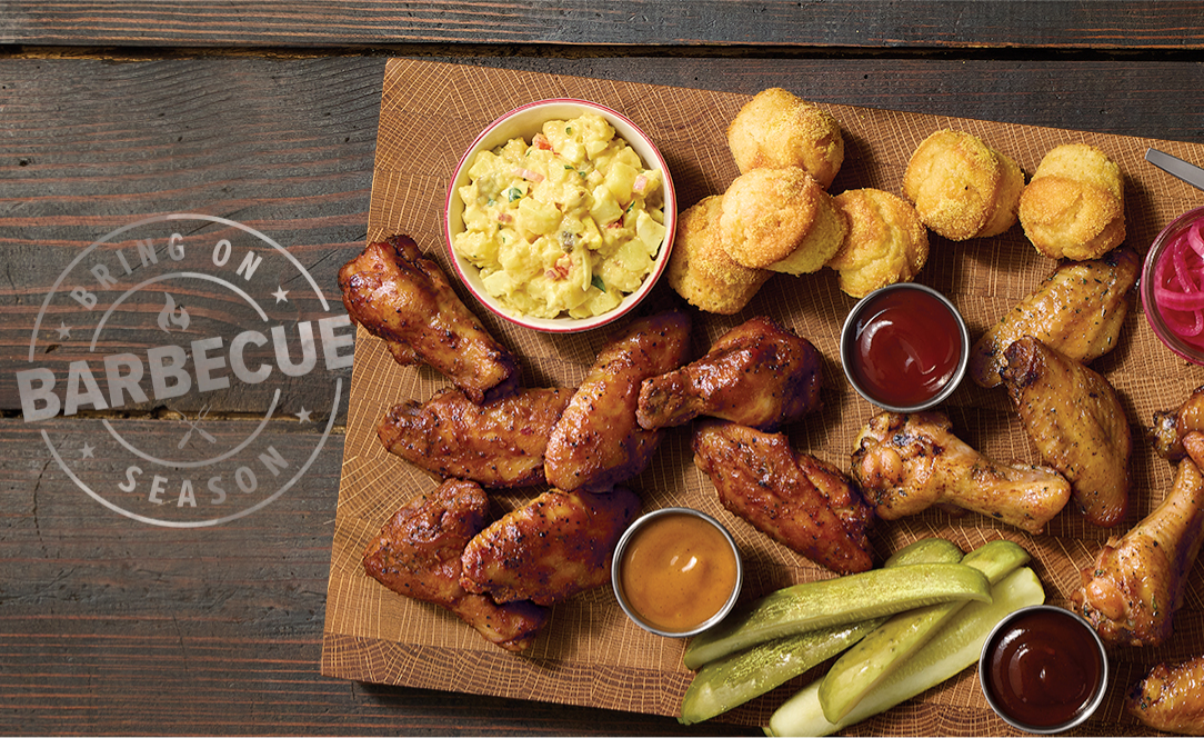A wooden platter featuring a chicken wings entrée next to a stamp that reads, “Bring On Barbecue Season.” 