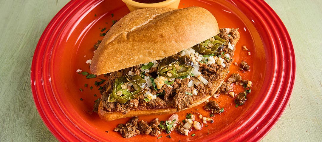 a plate with a large bun stuffed with sliced beef, onion relish and slice jalapeños        