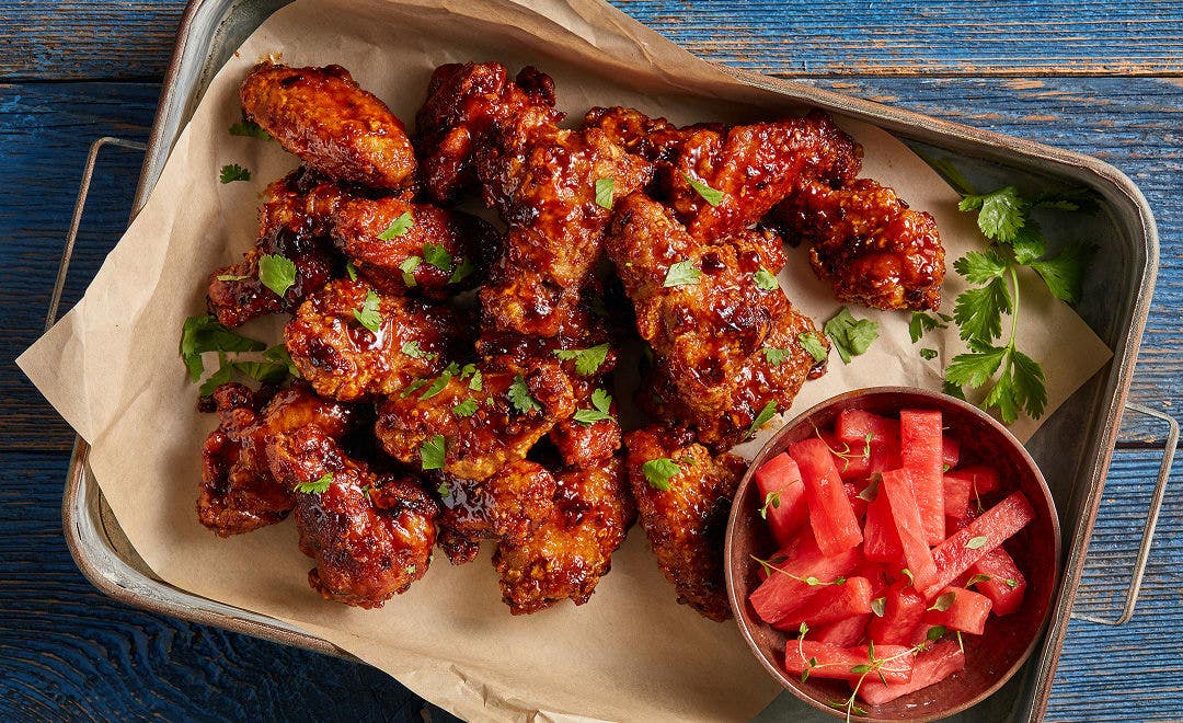 glazed bone-in breaded chicken wings with a ramekin of diced watermelon on the side