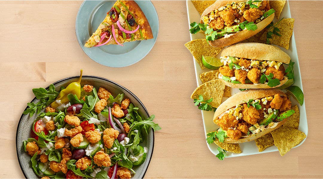 Food spread with salad, pizza, and sandwiches on a wooden table.