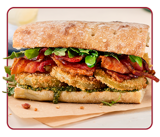 A whole-wheat bun stacked high with breaded fried green tomatoes, bacon and pesto  