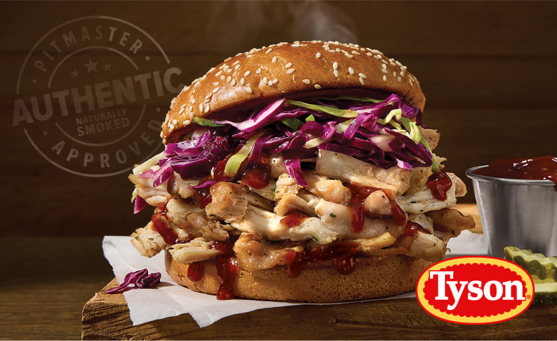 Pitmaster smoked chicken sandwich stacked on a sesame bun with sliced chicken, purple cabbage slaw, barbecue sauce, and Tyson branding visible