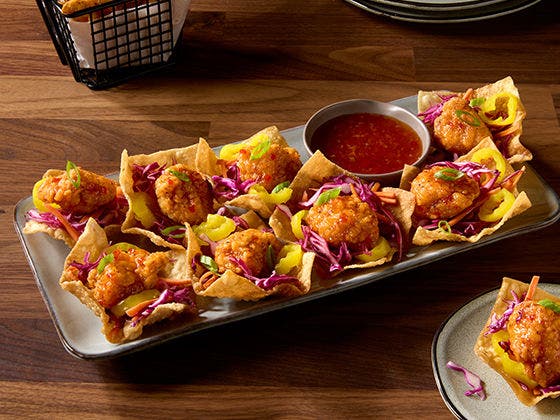 Plate of chicken wontons filled with sauced chicken breast chunks, cabbage slaw, jalapeño rings and scallion