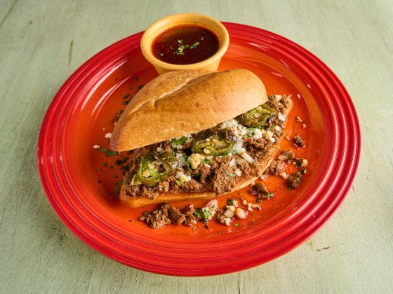 Birra cheesesteak with meat, cheese, and jalapeños on a red plate with a side of dipping sauce