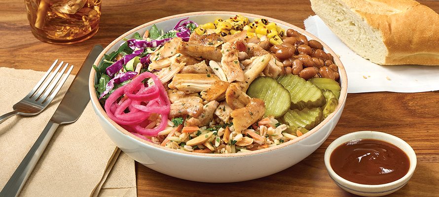 Bowl of smoked pulled chicken with corn, pinto beans, pickles, slaw, rice, and pickled onions, served with bread and barbecue sauce