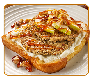 A white plate with thick toast topped with two sausage patties, pear slices and walnuts, drizzled with honey 