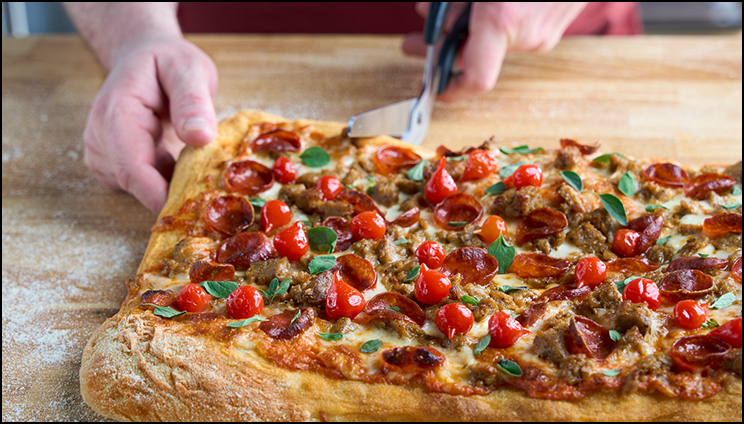 Pizza on a wooden table being cut