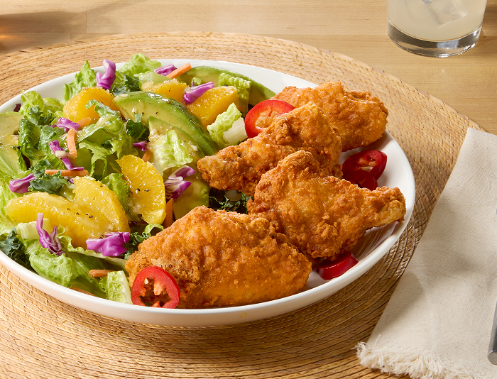 Plate of crispy fried chicken wings served with a fresh salad of mixed greens, orange segments, red cabbage, and sliced jalapeños on a table