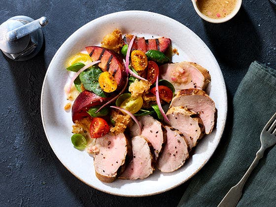 Pork tenderloin on a bread salad with fried croutons, tomatoes, shallots, spinach, basil and grilled plums