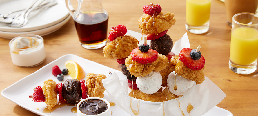Dessert-style skewers with fried chicken bites, strawberries, blueberries, and marshmallows drizzled with syrup on a platter