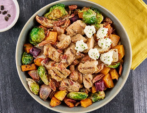 bowl topped with roasted root vegetables, caramelized butternut squash, Brussels sprouts, Boursin cheese, pecans, and black currant yogurt drizzle