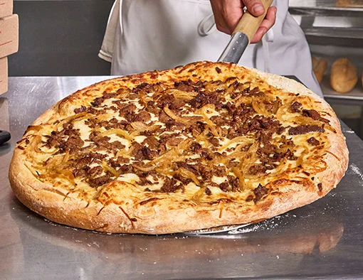 Steak and onion pizza being station on a metal table by a chef with a peel