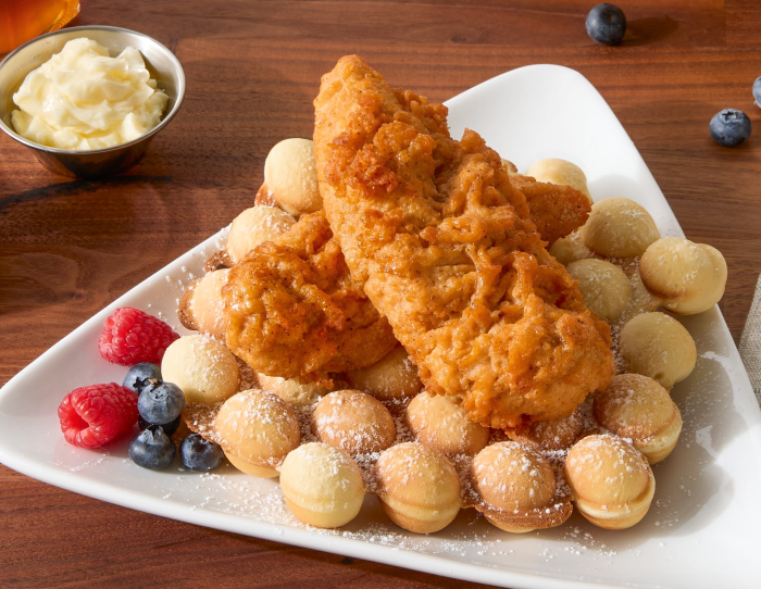 Hot honey breaded chicken tenderloins stacked over mini pancake bites, dusted with powdered sugar and served with berries and butter