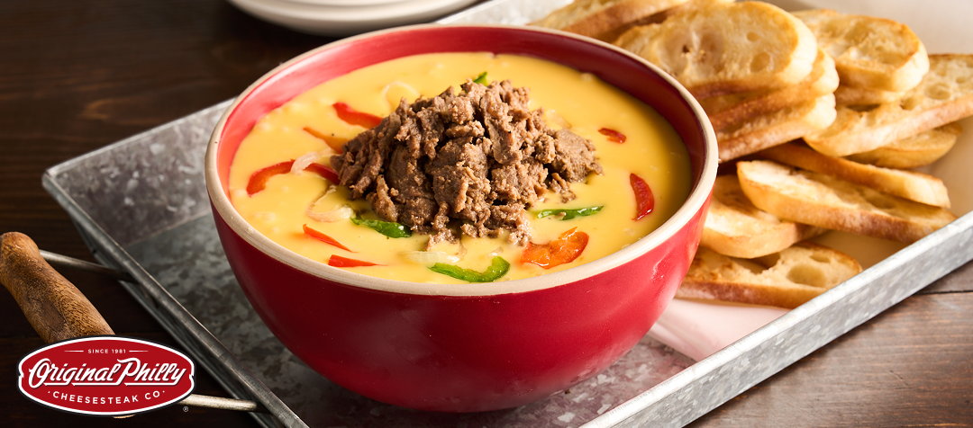 A serving tray with baguette chips and a bowl of cheese dip with bell peppers, onions and shredded beef. 