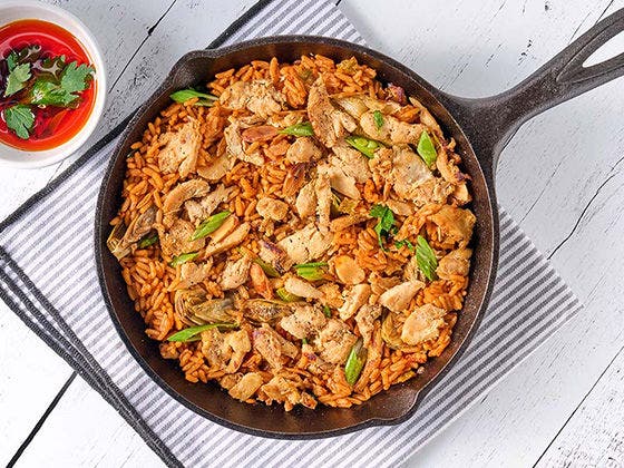Paella in a skillet with Sliced Chicken, artichoke hearts, peas, lemon zest, saffron rice, almonds and drizzle of smoked paprika oil.
