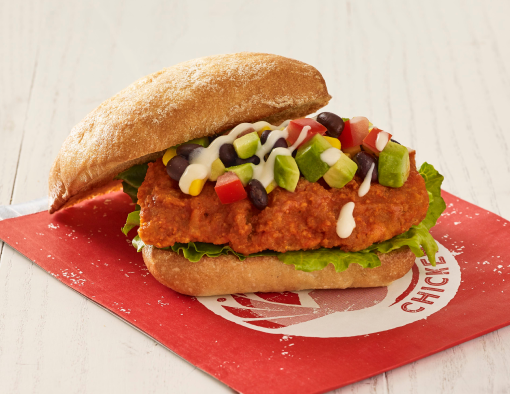 Breaded chicken breast on a whole-grain bun with avocado, tomato, corn, black beans and sauce 
