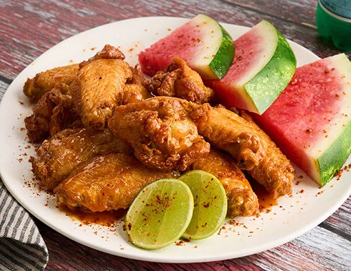 Chicken wings with tamarind glaze, served with chili lime watermelon and lime wedges on a white plate