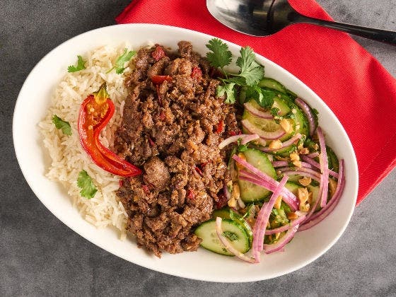 Rich, tender beef in a spiced coconut sauce served with steamed white rice garnished with cilantro and red bell pepper alongside a cucumber-onion salad. 